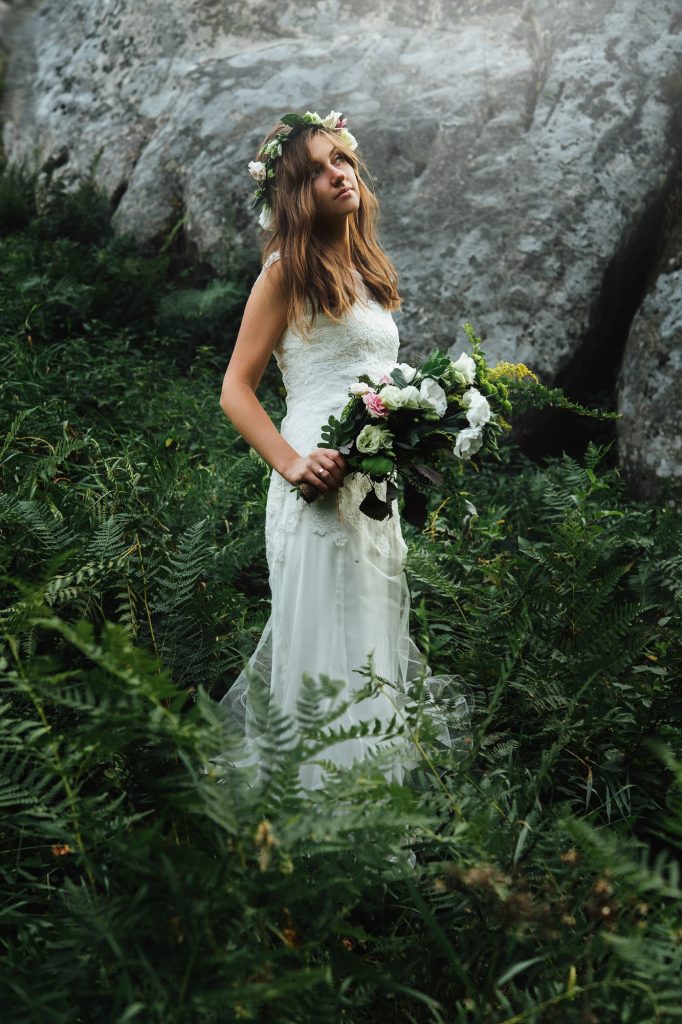 stylish sensual bohemian bride in a fairytale with bouquet on background of rocks in mountains